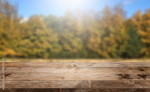 Autumn background, empty old rustic wood table with blur forest trees and sunlight, Autumn fall backdrop, banner for product display copy space, thanksgiving concept rustic textured grungy floor.