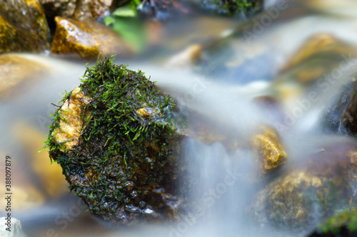 Mountain creek with water flowing (long exposure) and stone covered in moss