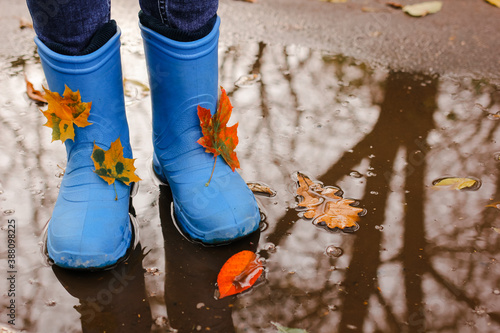 Teenager girl wearing blue rain boots jumping into a puddle on rainy autumn day. Closeup.