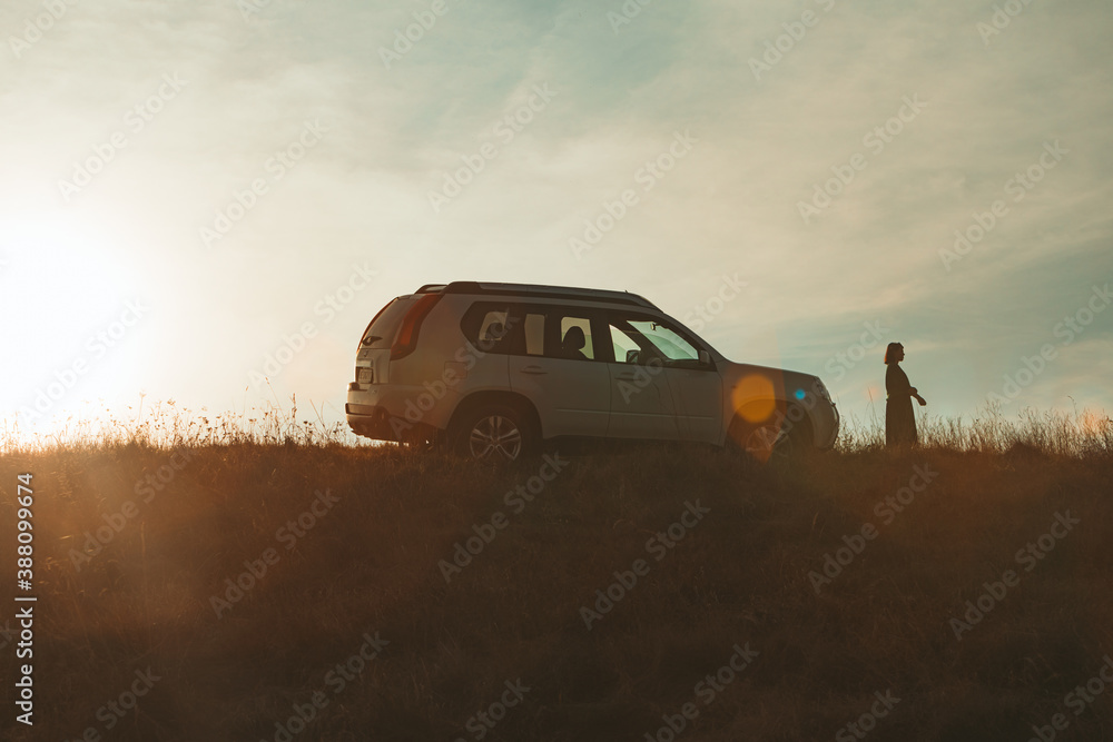 Fototapeta premium woman silhouette near suv car on sunset