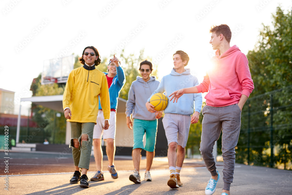 sportive young boys going to play basketball in the street, handsome teenagers have friendly talk while they are going at playground
