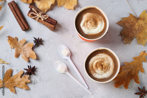 Two paper cups with tasty pumpkin latte and spice on gray table with autumn leaves. Top view. Closeup.