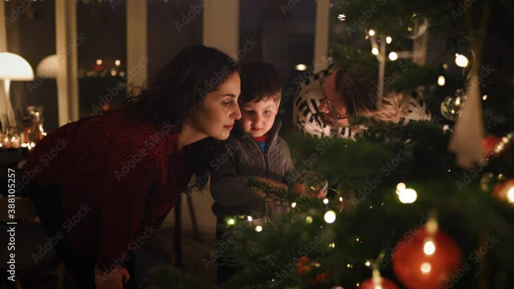 Christmas holidays. A boy looking at the lights on the Christmas tree together with his parents. Interior shot of a family home decorated for Christmas.
