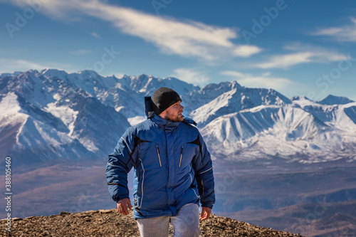 View of a tourist walking in the mountains. White snowy mountain ridge and beautiful blue cloudy sky as a background and slightly out of focus. Altai mountains, Siberia, Russia