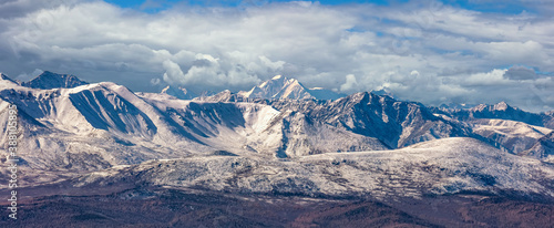 Scenic panoramic aerial view of snowy mountain peaks and slopes of North Chuyskiy ridge. Beautiful cloudy blue sky as a background. Altai mountains, Siberia, Russia photo