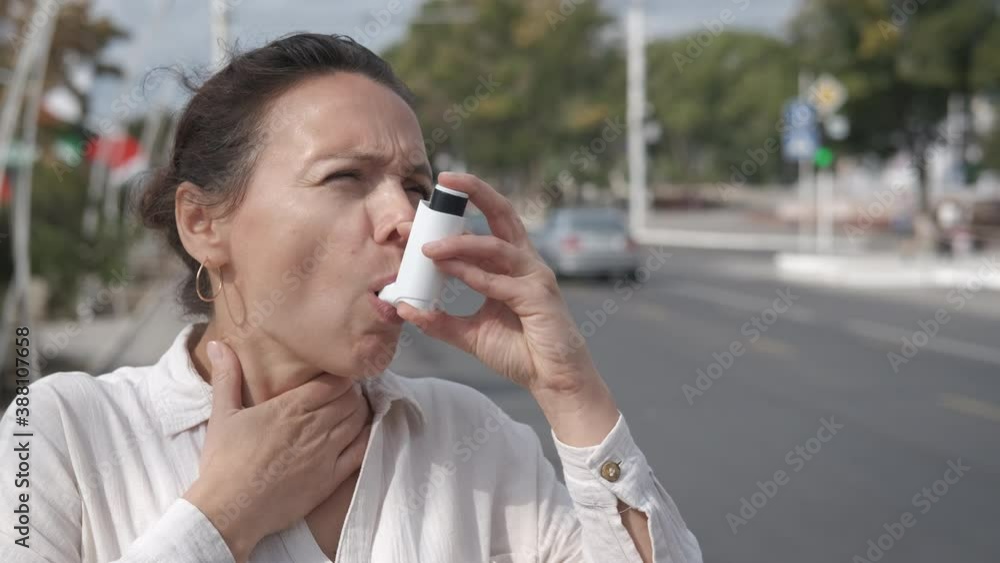 Woman with inhaler in the city street. A woman has an asthma attack and use an inhaler by the road with traffic. Woman with inhaler in the city street. A woman has an asthma attack and use an inhaler by the road with traffic.