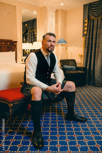 handsome mature courageous stylish man (gay) scotsman in kilt in fancy hotel room. Style, fashion, lifestyle, culture, travel, ethnic concept.