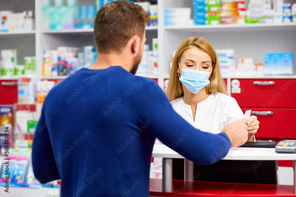 Obraz premium young professional druggist give medications to customer in modern drugstore, consult and recommend, wearing medical mask protecting from coronavirus covid-19