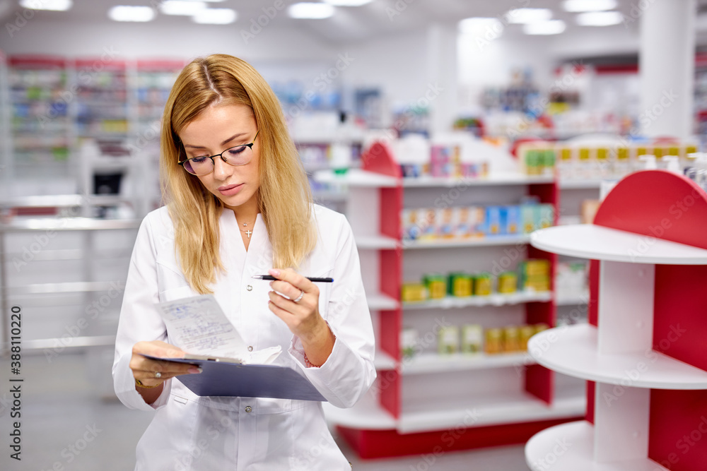 young good-looking woman pharmacist searching for medication on pharmacy shelves, examine and check assortment of drugs in pharmacy