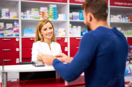 young beautiful caucasian pharmacist is working with customer in modern drugstore, serve the client, wearing white medical gown