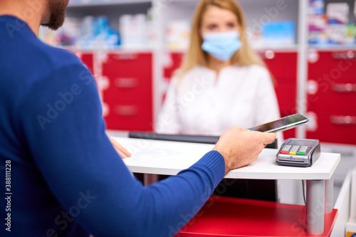 cropped customer pay for drugs in pharmacy, focus in hand with smartphone and terminal for payment