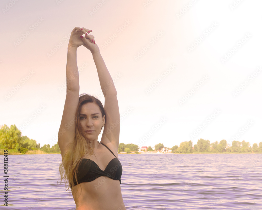 The bright sun shines over a girl in a swimsuit on a lake in the water