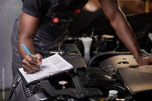 afro american guy repairing car hood and make notes in notebook, alone, wearing uniform