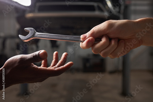 two young diverse mechanics hands giving, sharing tool to each other. automotive craftsman during work, help, cooperate. car service concept