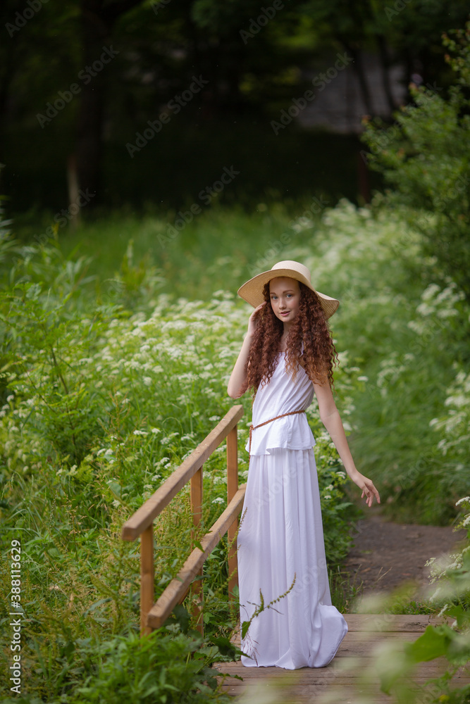 Cute red girl in straw hat on a flowering clearing at a picnic with fruit Cute red girl in straw hat on a flowering clearing at a picnic with fruit