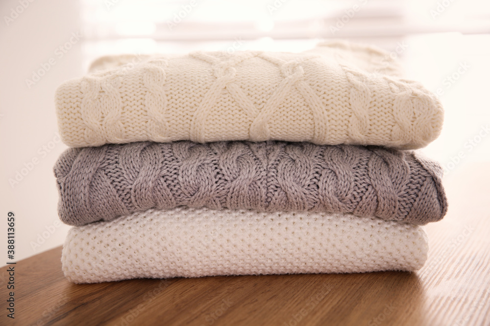 Stack of folded warm sweaters on wooden table indoors, closeup Stack of folded warm sweaters on wooden table indoors, closeup