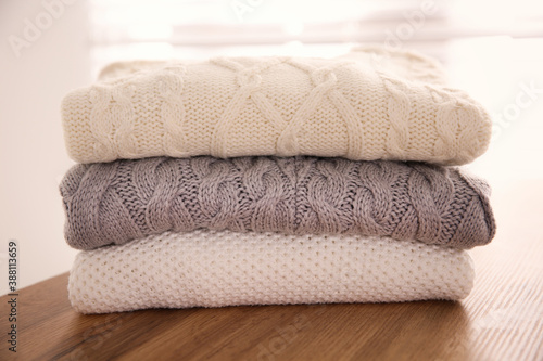 Stack of folded warm sweaters on wooden table indoors, closeup