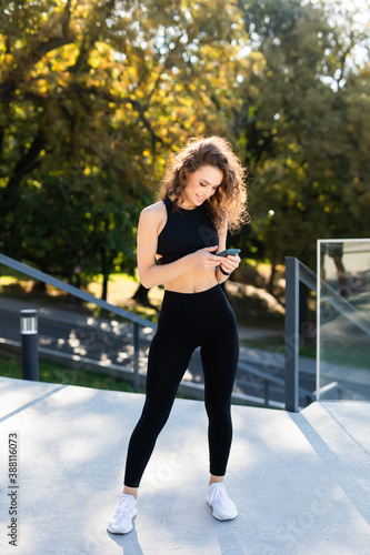 Young fitness woman use phone before running outdoors in the park