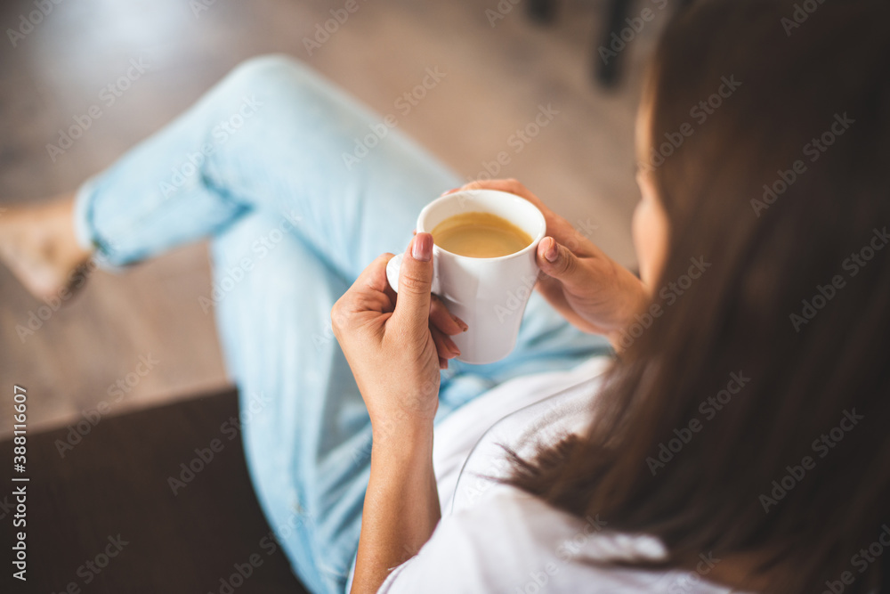 Top view of Caucasian young woman holding coffee cup while sitting on sofa at home
