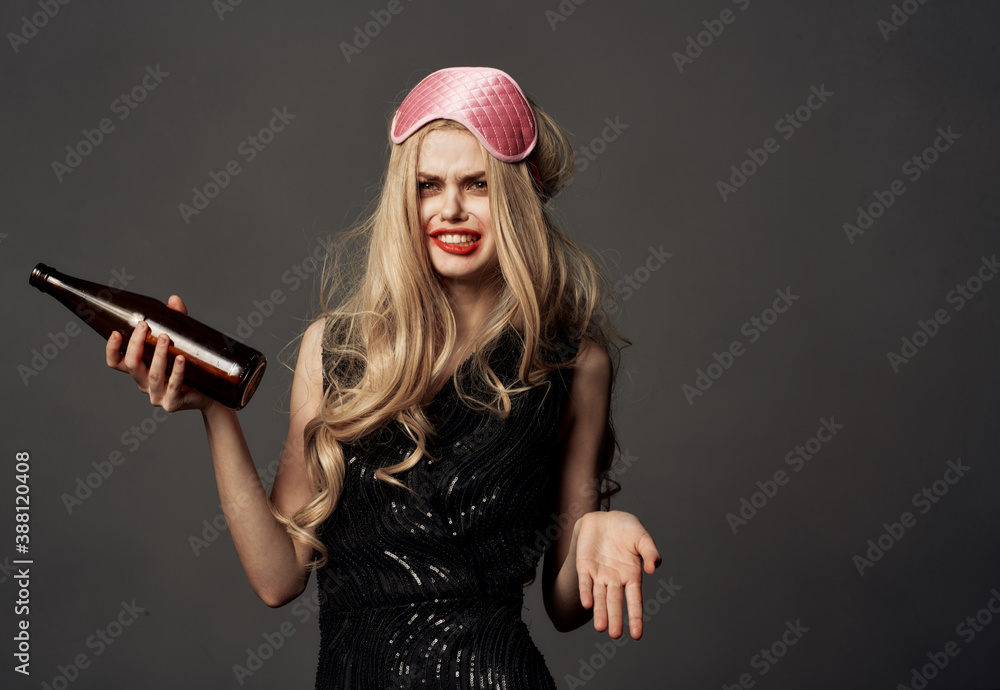 Woman holding a bottle with alcohol in her hands on a gray background black dress sleep mask Woman holding a bottle with alcohol in her hands on a gray background black dress sleep mask