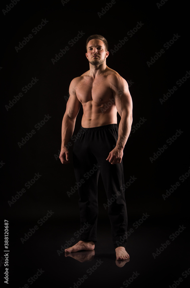 Naklejka premium Strong athletic man showes naked muscular body on a dark background.