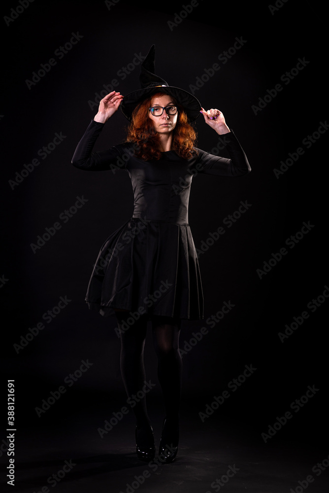 Young woman in black dress and witch hat on a black background. Young woman in black dress and witch hat on a black background.