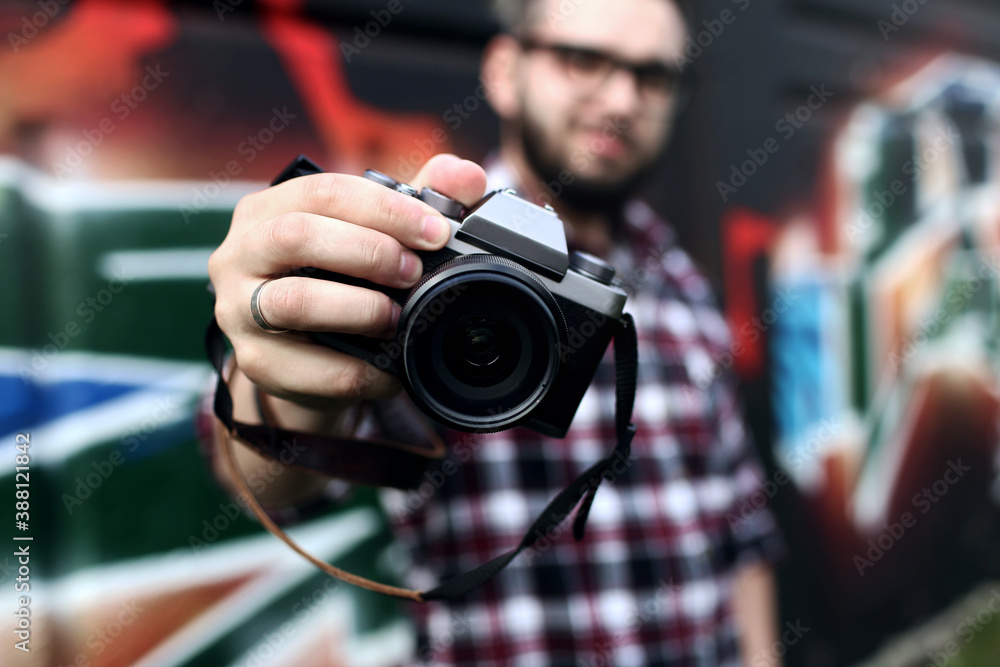 Hipster guy holding a retro photo camera close-up on his outstretched hand. Blurred background Hipster guy holding a retro photo camera close-up on his outstretched hand. Blurred background