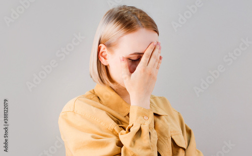 Embarrassed annoyed adult woman hiding face bend head down, facepalm, smirk irritated, not looking friend acting weird, feel humiliated uncomfortable, standing gray background