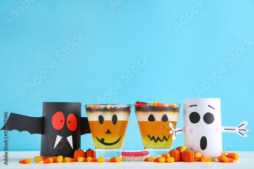 Halloween jelly in glasses with candies and paper ghosts on blue background