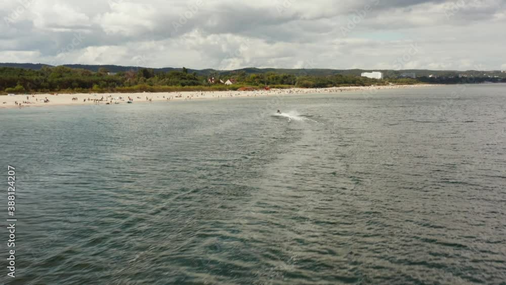 Aerial View in a water ski with a woman and a man riding in the sea near the beach on a sunny summer day. Aerial View in a water ski with a woman and a man riding in the sea near the beach on a sunny summer day.