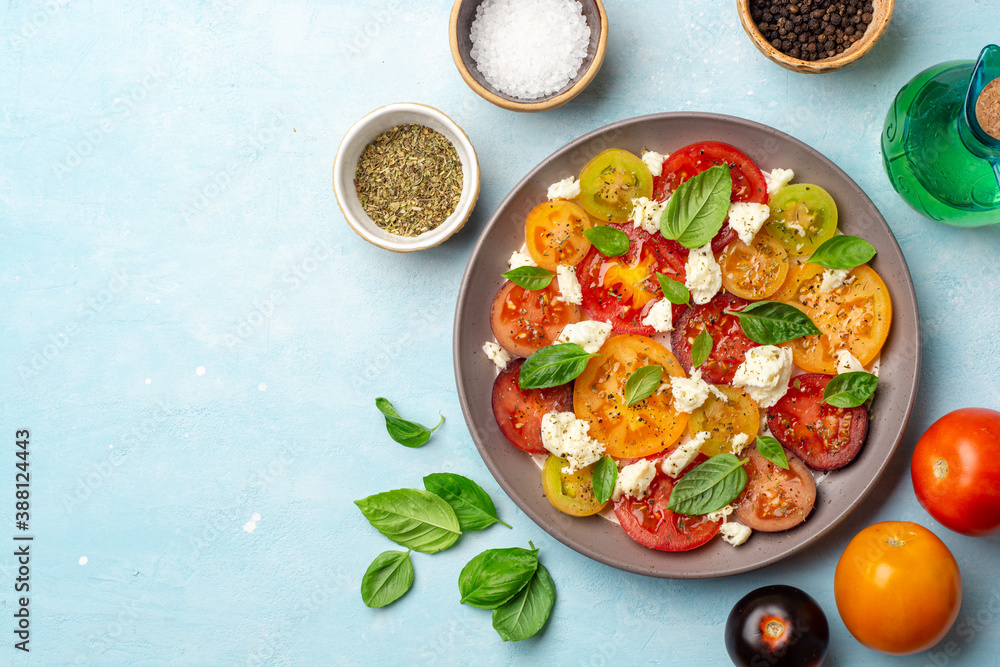 Italian caprese salad with varicolored tomatoes, mozzarella cheese, basil leaves, spices and olive oil in plate on concrete background Italian caprese salad with varicolored tomatoes, mozzarella cheese, basil leaves, spices and olive oil in plate on concrete background
