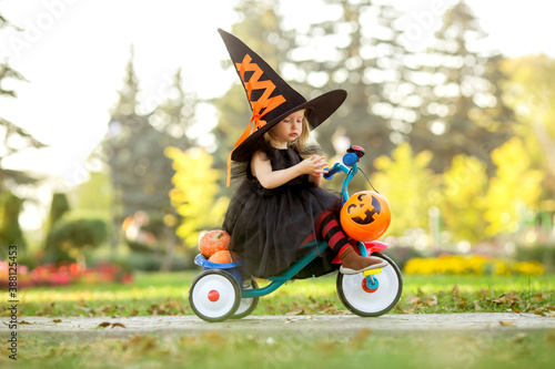 cute little girl in a witch's costume rides down the street on a children's bike with pumpkins and candy © КРИСТИНА Игумнова