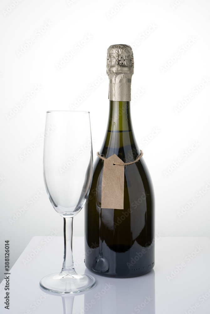 A bottle of alcohol with a label on a string and a glass on a light background. Side view. The concept of festive drinks.