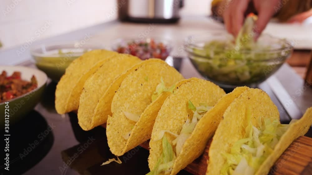 Woman hand stuffing hard taco shells - adding the lettuce filling, camera orbit, close up, slow motion. Phases of making tacos.