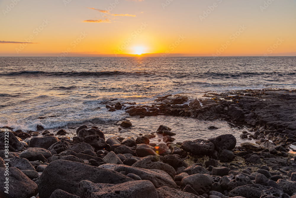 Tropical orange sunset over lava rock shoreline and ocean