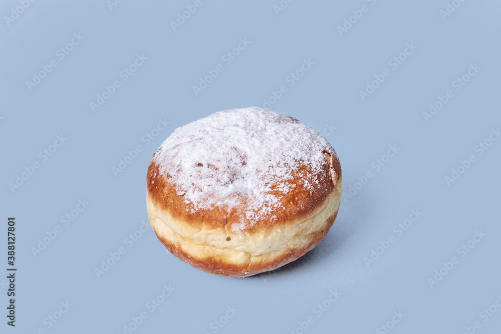The view from the top. Delicious doughnut with filling, sprinkled with powdered sugar. Isolated on a blue background. High-calorie food. The view from the top. Delicious doughnut with filling, sprinkled with powdered sugar. Isolated on a blue background. High-calorie food.