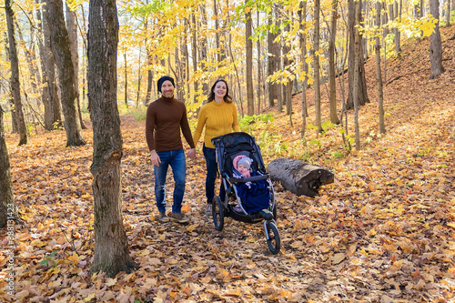 Baby daughter and her parents in the autumn season in park walking with the stroller