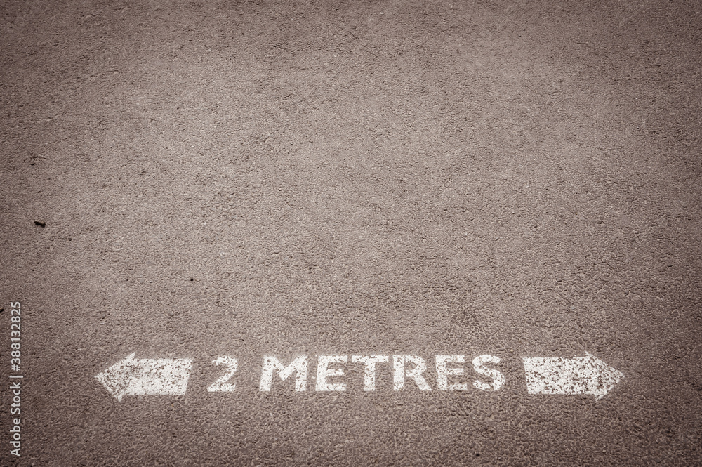Fototapeta premium Social distancing road painted sign recommending staying 2 metres apart