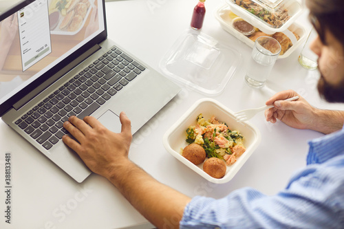 Man having lunch break in office, eating takeaway meal and signing up for food delivery website