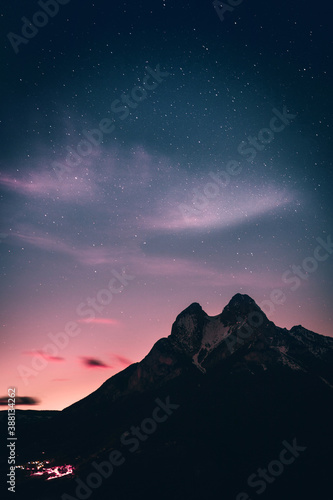 Peak of a snowy mountain and the lights of a small town at dusk with stars at blue hour and the evening lights. Pedraforca Mountain, Gósol, Bergueda, Barcelona, Catalonia, Spain.