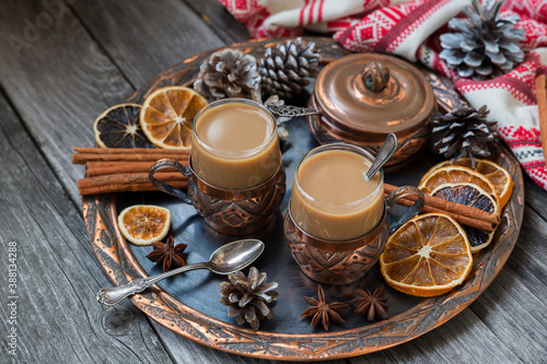 Copper cups of hot coffee with cream, with cinnamon, anise on a copper tray and a wooden background.