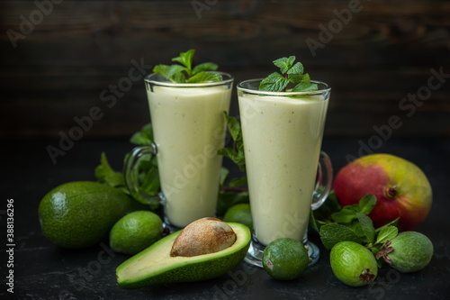 Two glasses of fruit smoothie from mango, avocado, feijoa and cream on a dark background