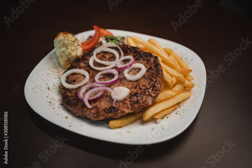 baked barbecue with french fries and salad and onion on a plate, Serbian dish "Pljeskavitsa"