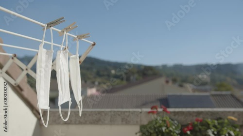 Three white masks hang in a clothesline with a soft wind in the terrace over a blurred rural environment