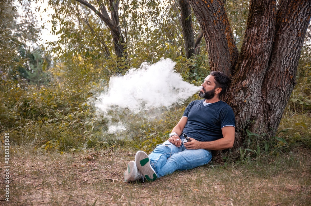 Stylish man enjoying an electronic smoke device in a forest clearing. Vaping activity. Stylish man enjoying an electronic smoke device in a forest clearing. Vaping activity.
