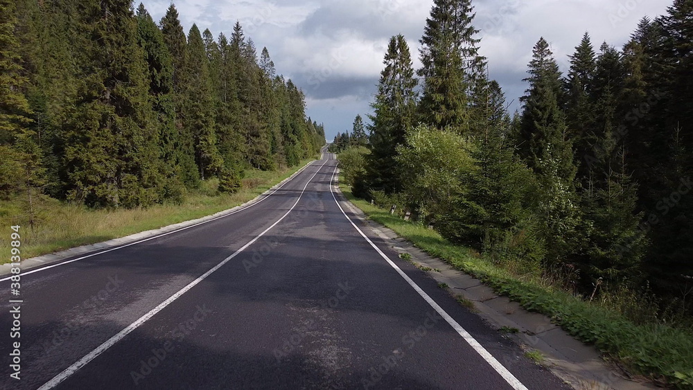 Aerial low air flight over mountain perfect asphalt highway road and meadow at sunny summer morning. Near green trees. Fast horizontal movement with sun rays. Aerial low air flight over mountain perfect asphalt highway road and meadow at sunny summer morning. Near green trees. Fast horizontal movement with sun rays.