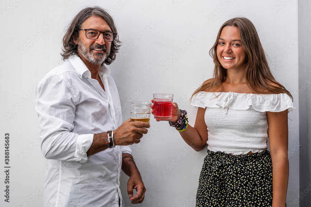 Smiling father toasting drinks with daughter while standing against wall Smiling father toasting drinks with daughter while standing against wall