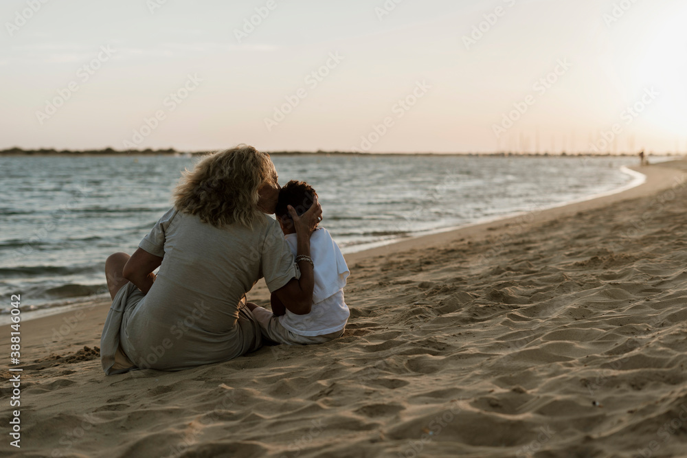 Grandmother kissing grandson while spending leisure time at beach during sunset Grandmother kissing grandson while spending leisure time at beach during sunset