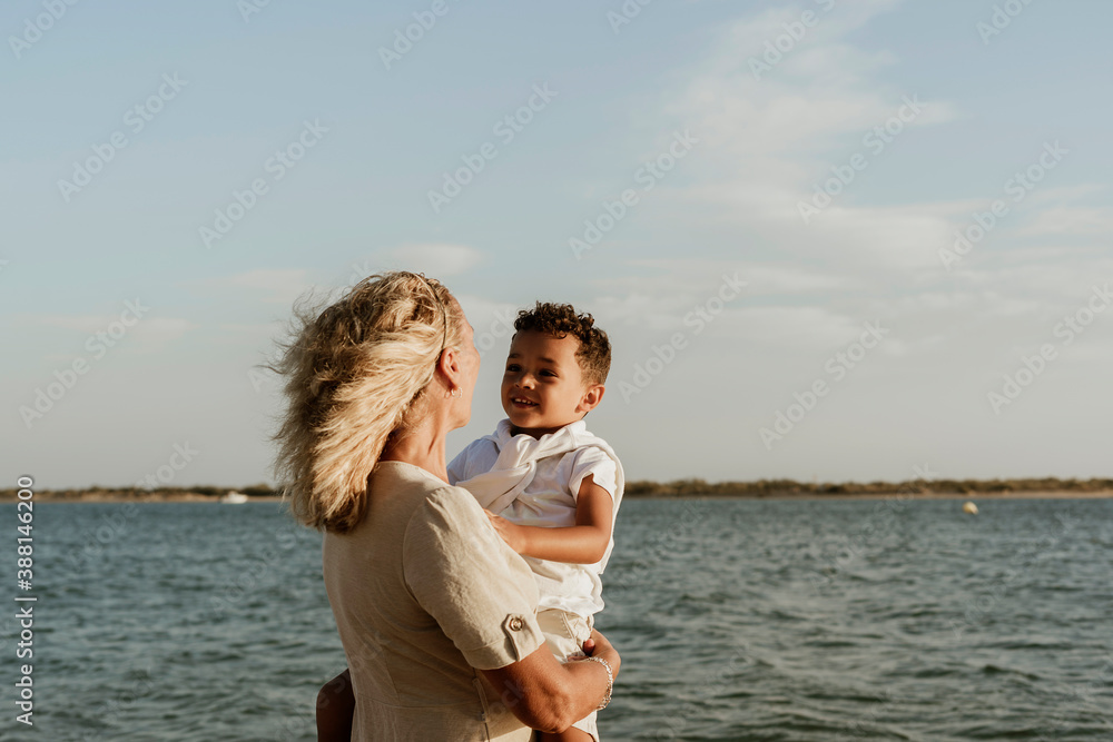 Grandmother picking up grandson in arms while standing at beach Grandmother picking up grandson in arms while standing at beach