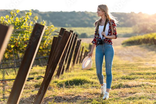 Young woman holding camera while walking at vineyard photo